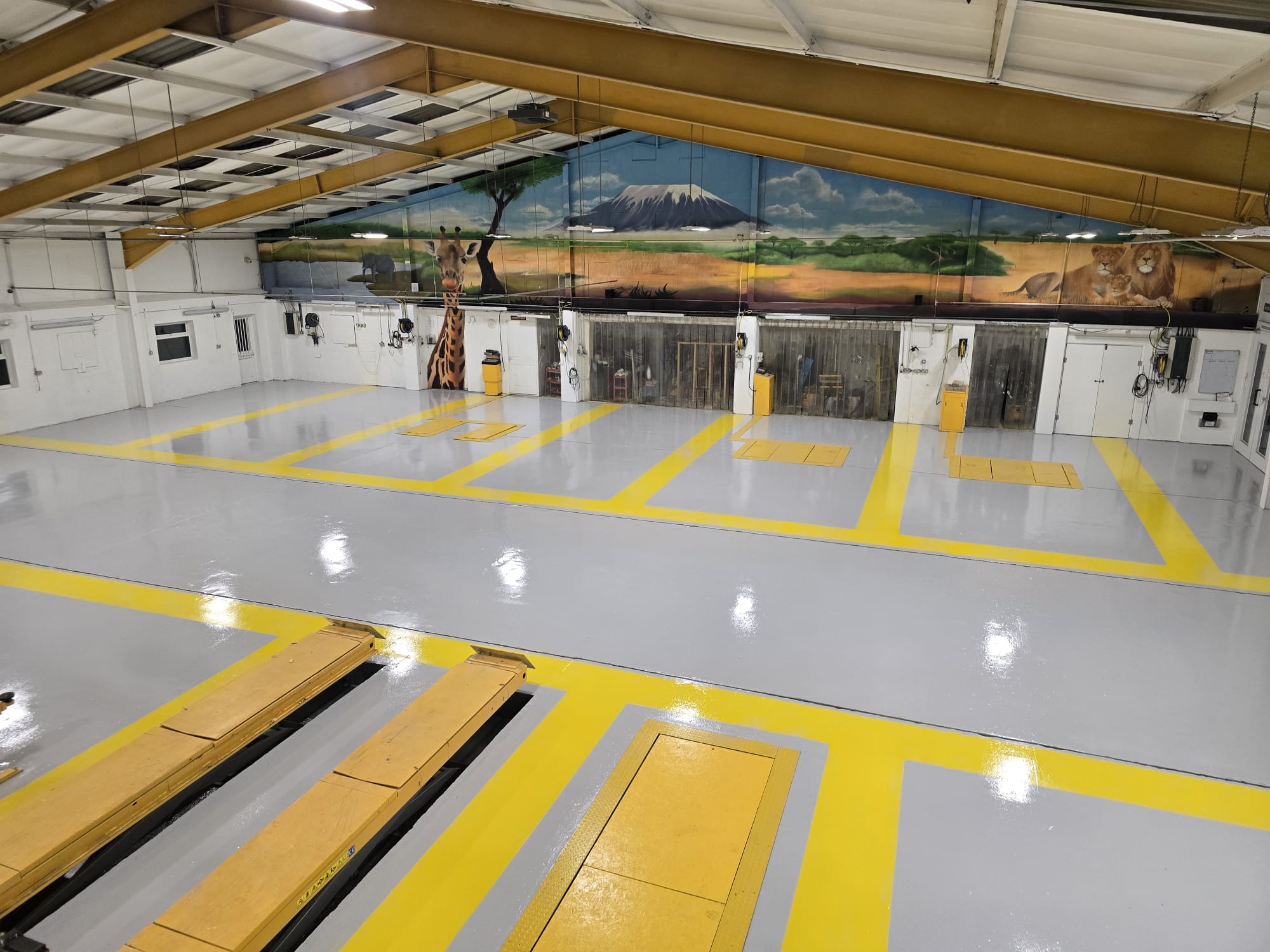 A grey epoxy resin flooring system with yellow line marking paint demarcating car bays